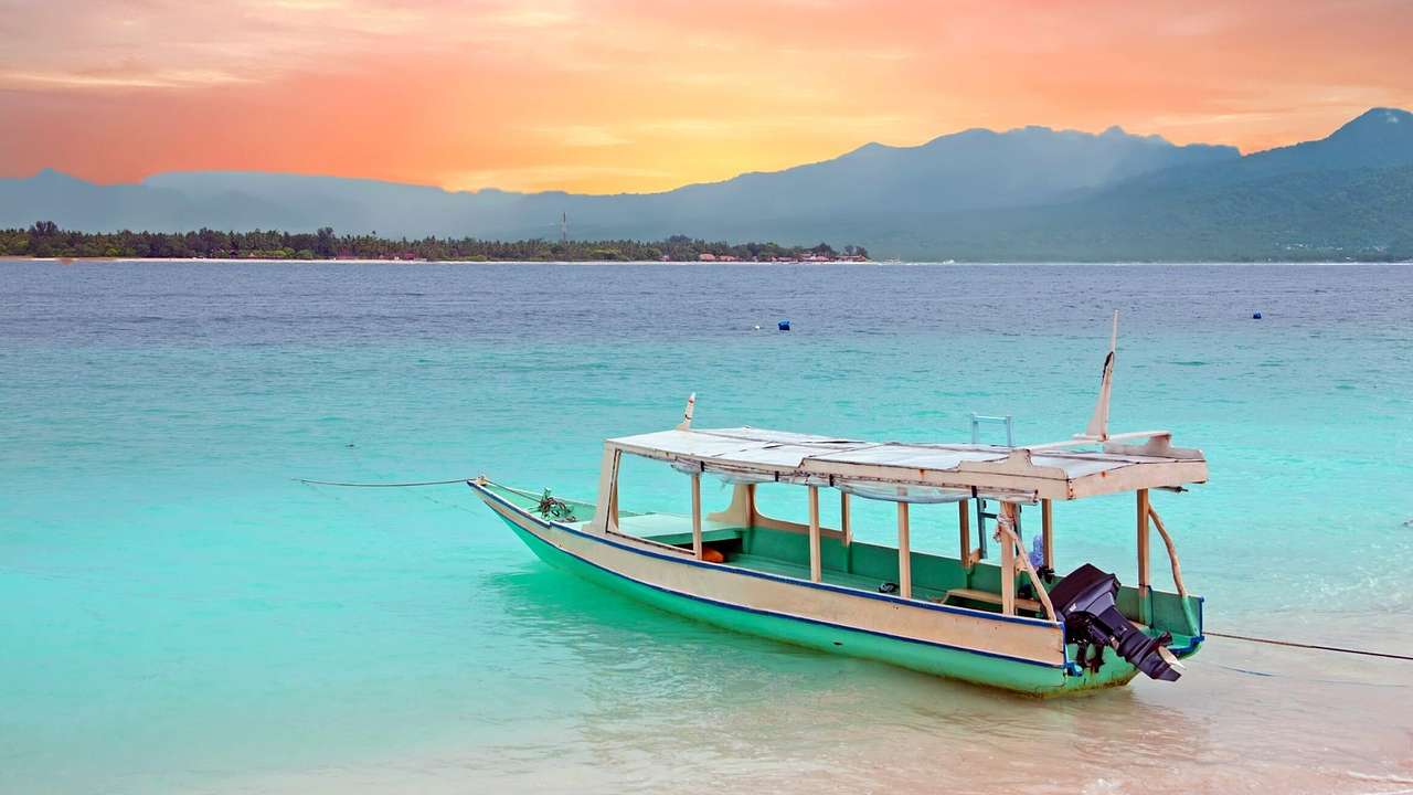 A traditional white boat on a seashore with hazy mountains at the far back, at sunset