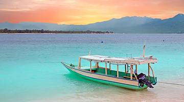 A white boat on a seashore and hazy mountains at the far back, at sunset