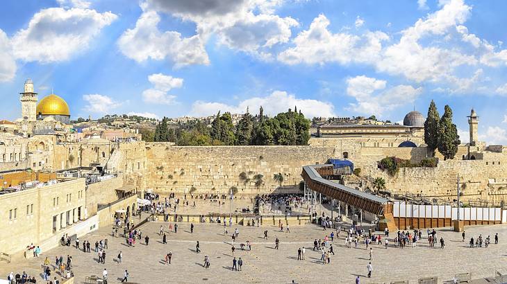 An ancient stone paved area with stone walls with a large golden dome in the distance