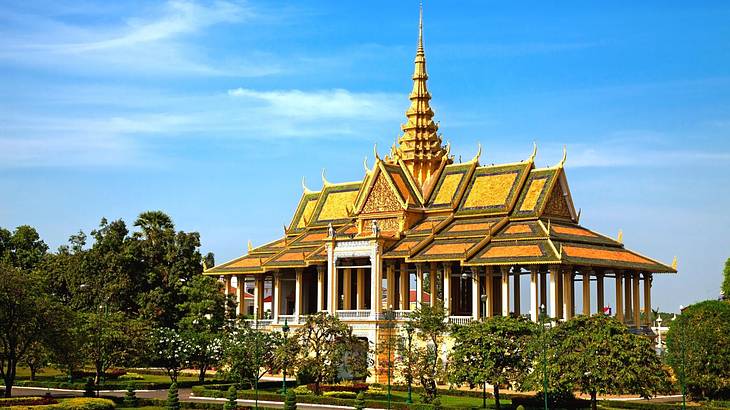 A palace-like building with a golden roof and a spiky tower, surrounded by greenery