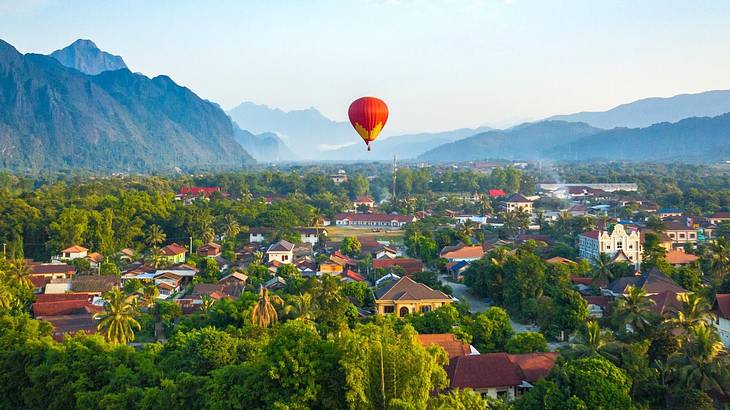 A hot air balloon over a town with lush greenery and houses, against hazy mountains