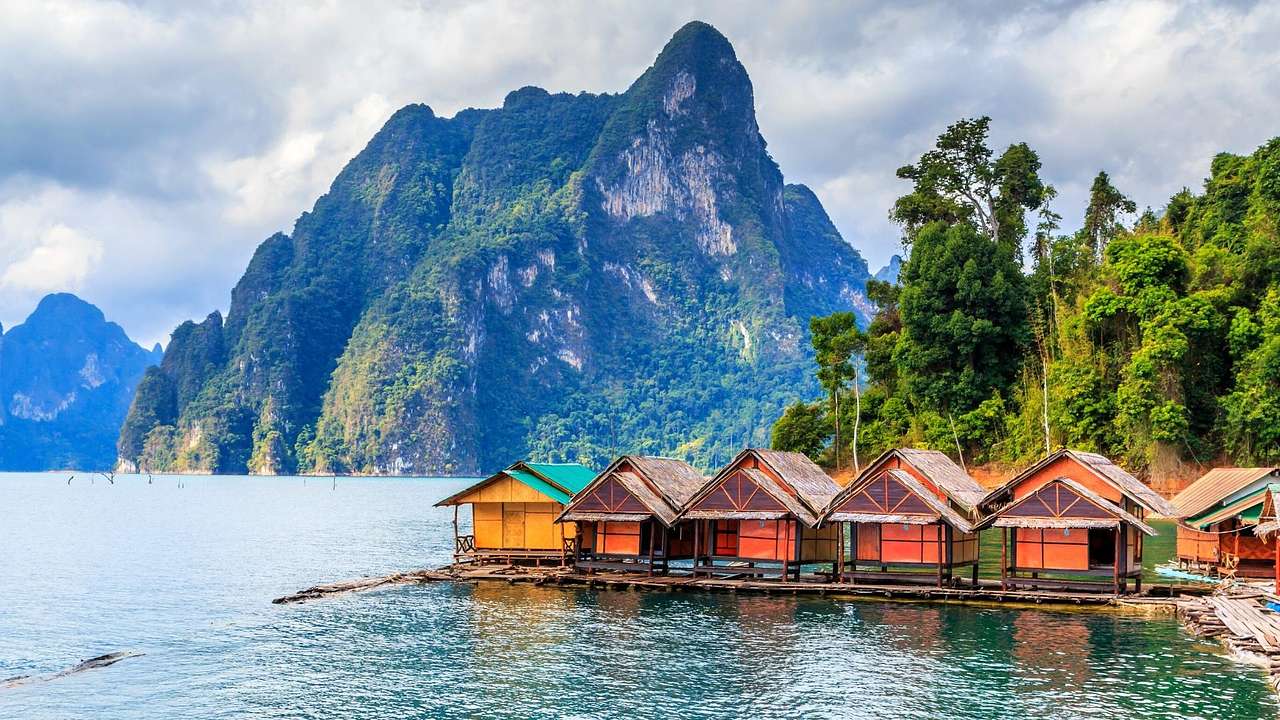 Multi-color wooden huts lined up against trees and a mountain surrounded by water