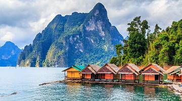 Multi-color wooden huts lined up against trees and a mountain surrounded by water