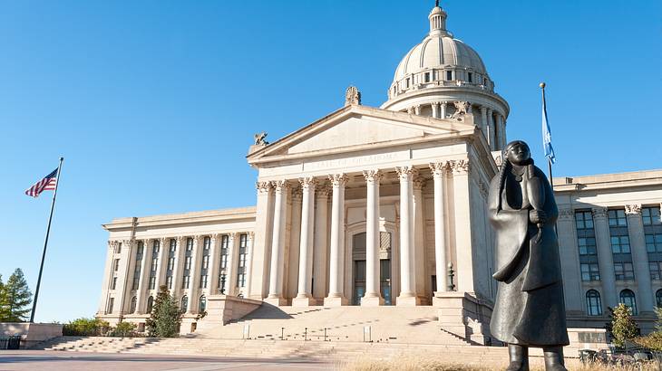 A bronze statue of an Indian in front of a white building with a dome and columns A bronze statue of an Indian in front of a white building with a dome and columns