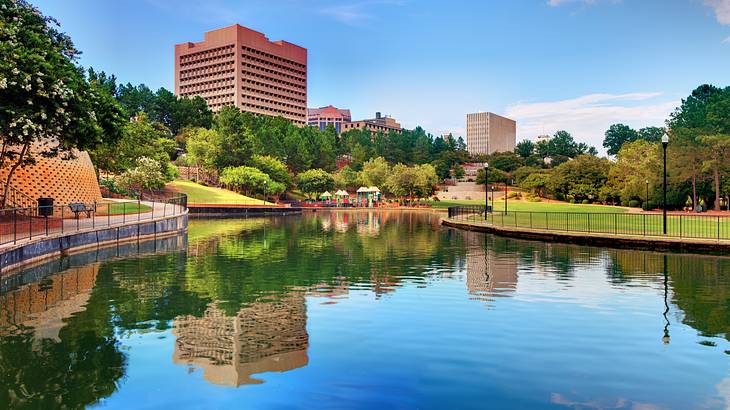 Buildings, trees, and sky reflected in a lake in the middle of a park