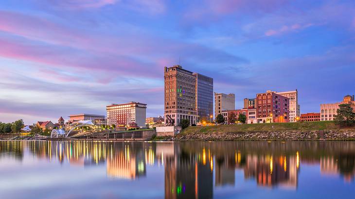 Tall buildings reflecting on a body of water against a sunset with pinkish-blue sky Tall buildings reflecting on a body of water against a sunset with pinkish-blue sky