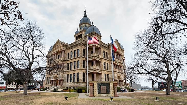 A brick building with domed roofs next to US and Texas flags and bare winter trees