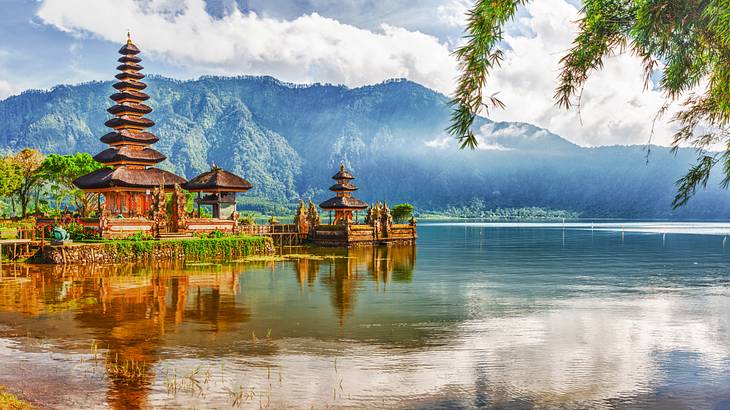 A tall temple in Bali next to a lake and mountains under a blue sky with clouds