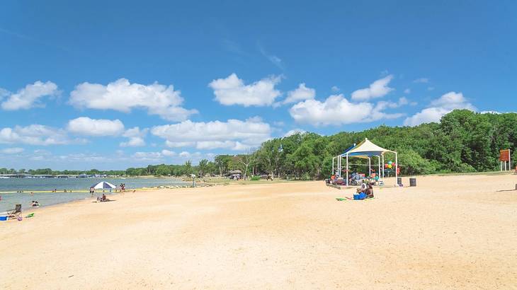 A sandy beach with people sitting on it next to the water under a blue sky with cloud