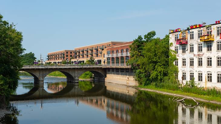 A river next to grassy banks and brown and white brick buildings on a nice day