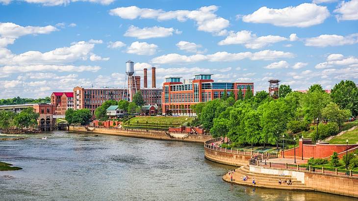 A river next to trees, a small park, and red brick buildings