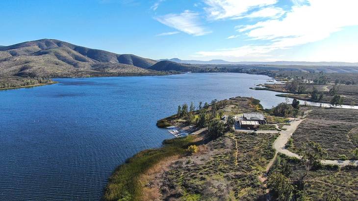 A lake with greenery-covered land and mountains around it under a blue sky