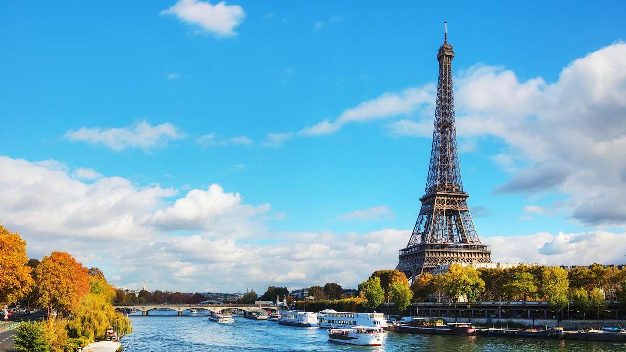 The Eiffel Tower as seen behind trees and the River Seine with boats on it