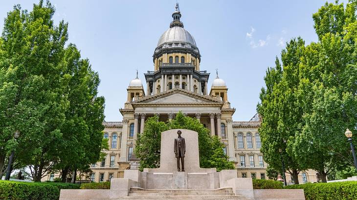 A political building with a domed roof and a statue of Lincoln and trees next to it