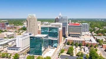 A view of the Raleigh skyline with buildings and trees under a blue sky with clouds
