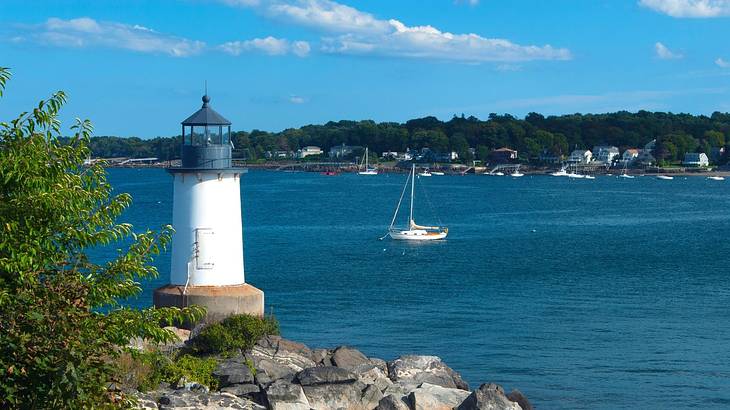 A white lighthouse with a black top sitting on the shore of a bay