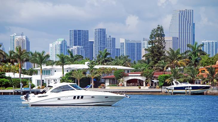 A white boat in front of a city skyline filled with palm trees and tall buildings A white boat in front of a city skyline filled with palm trees and tall buildings