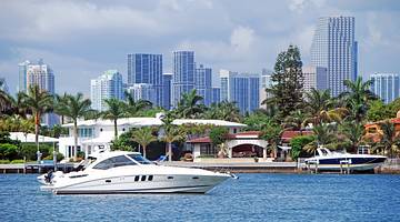 A white boat in front of a city skyline filled with palm trees and tall buildings