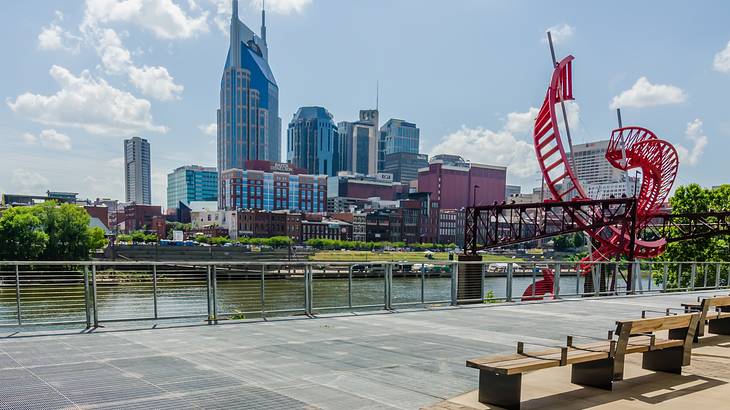 Benches looking over a river at a city skyline with a red sculpture nearby