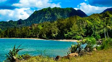 Turquoise sea water with a beach, greenery, and greenery-covered mountain surrounding
