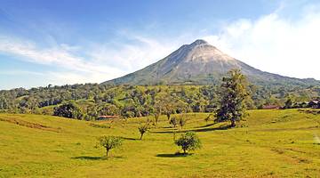 A volcano peak in the background with green tree-filled hills in the foreground