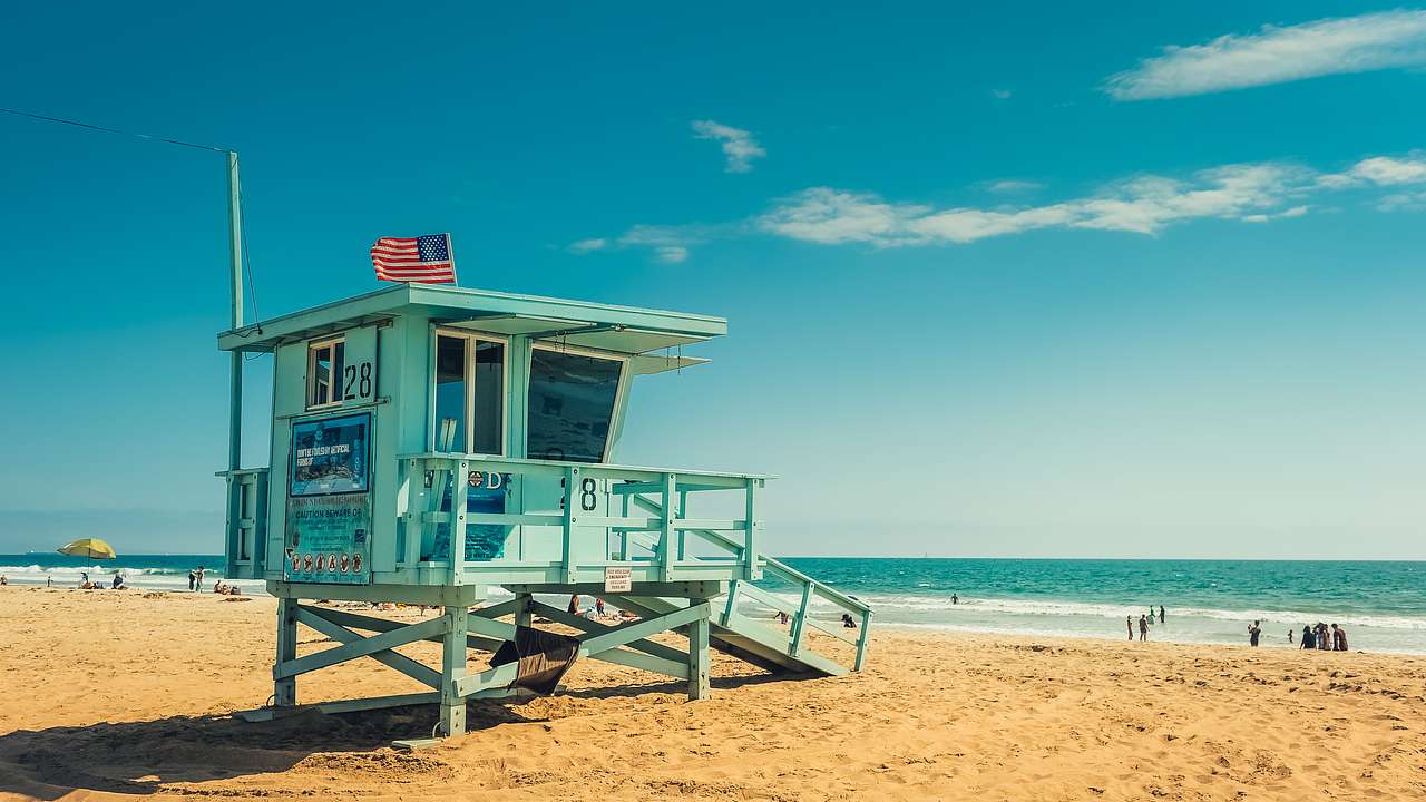 Blue lifeguard house with a white, red, and blue flag on a golden sandy beach