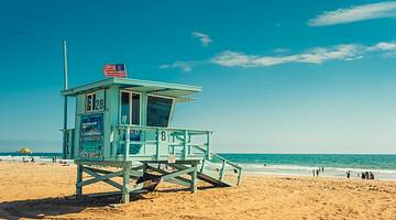 Blue lifeguard house with a white, red, and blue flag on a golden sandy beach