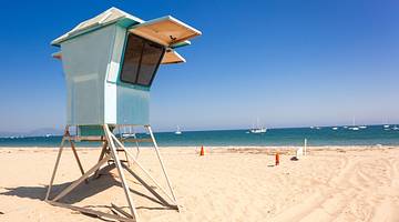 White sandy beach, with a light blue hut on stilts, facing blue water and sky