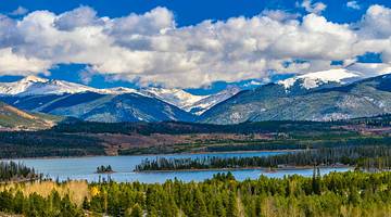Mountain range partly covered with snow & trees and a body of water in front Mountain range partly covered with snow & trees and a body of water in front