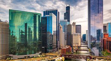 A river winding through many modern glass buildings under a partly cloudy sky