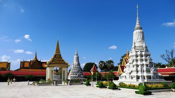 A tower-like Asian sculpture next to smaller structures and a square with some bushes