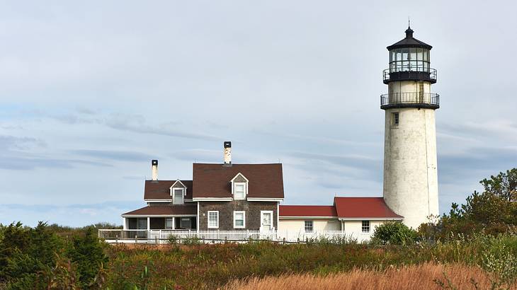 A white and black lighthouse and a small building on a grassy hill