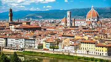 Sunny aerial view of renaissance buildings facing a river with mountains in the back