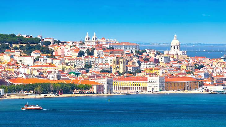 A view of a coastal city with white buildings with orange roofs next to the water