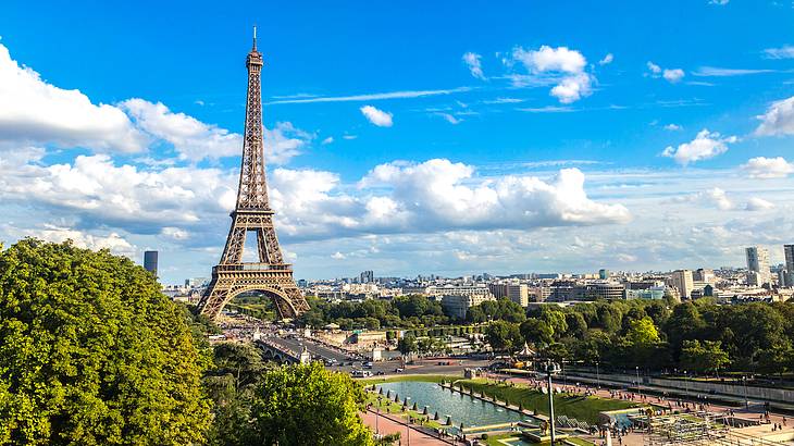 The Eiffel Tower facing a canal surrounded by buildings and greenery on a sunny day