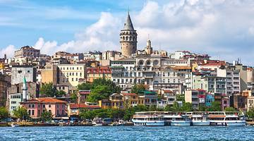A city with a tower and trees on a hill next to the water