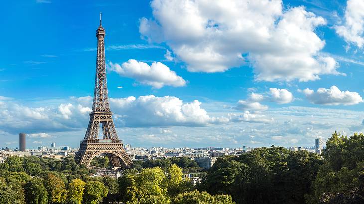 A massive pointy tower surrounded by shorter buildings, greenery, and a sunny sky