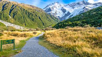 Snow-capped mountains at the back with a gravel path and grassy field in front