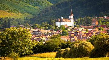 Transylvania itinerary - A church in between homes and green rolling hills, Sibiu
