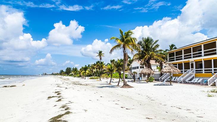 A white sand beach with palm trees in front of beach houses under a partly cloudy sky