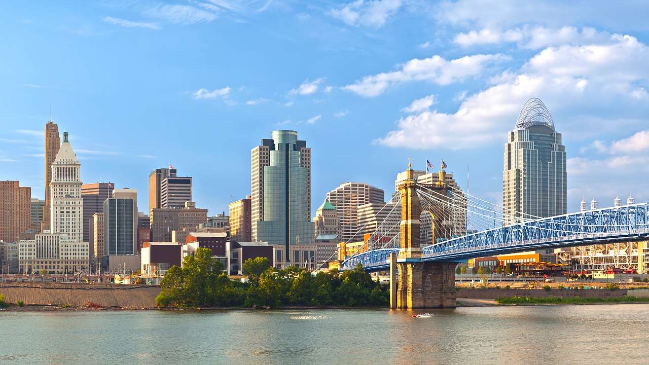 A river with a bridge over it next to a city skyline under a blue sky with clouds