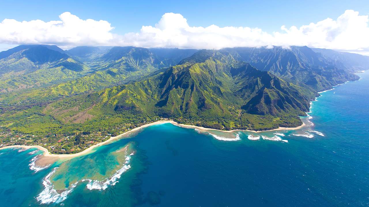 Top view of sandy coastline where green mountains meet deep blue ocean waters