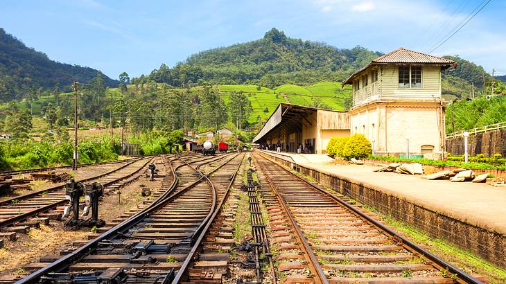 Several railroad tracks with a building on the right and mountains at the back