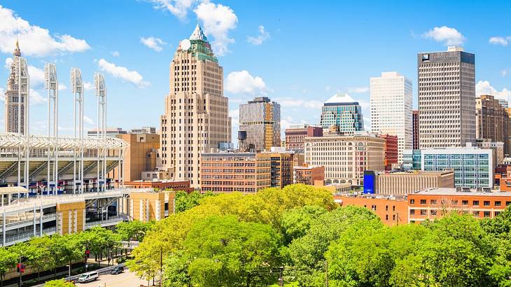 A city skyline with greenery in front of it under a blue sky with clouds