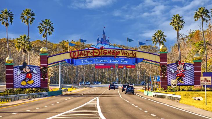 A road leading to a sign that says "Walt Disney World" next to palm trees