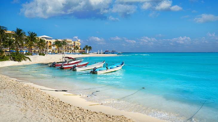 Bright blue ocean water with boats on it, next to a sandy beach with small buildings