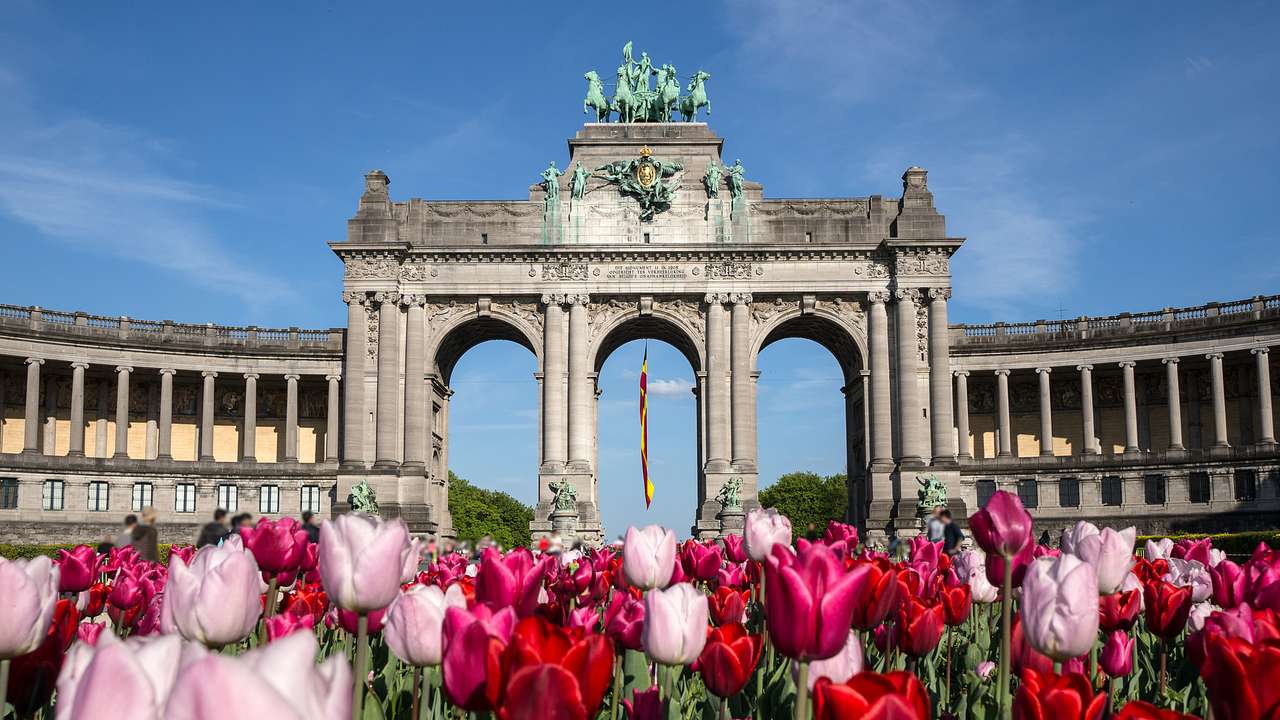 A large stone structure with three large arches and red tulip flowers in front