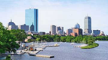 A view of a city skyline with a body of water and green trees in front of it A view of a city skyline with a body of water and green trees in front of it