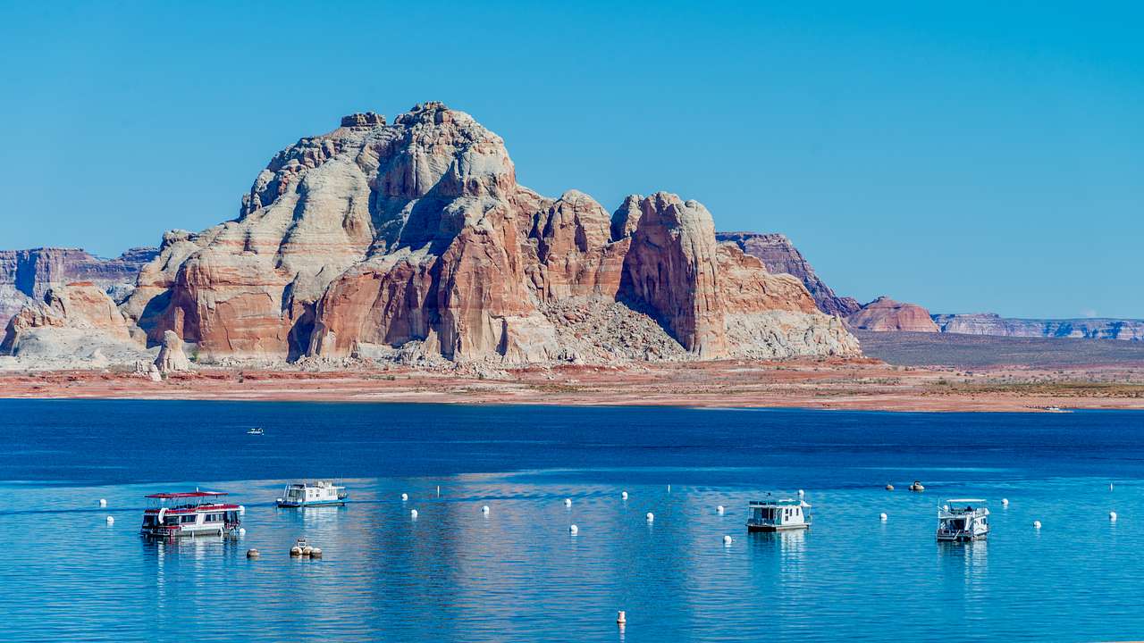 A striped rock mountain and water in front with boats on it under a blue sky