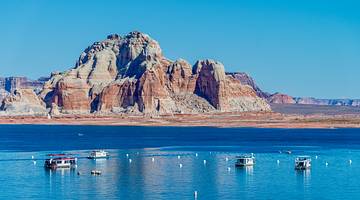 A striped rock mountain and water in front with boats on it under a blue sky